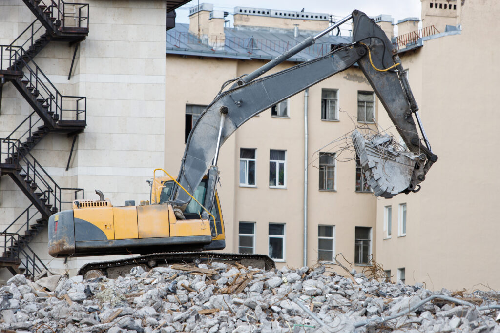 Abriss des Gebäudes des ehemaligen Hotels für den Neubau mit einem speziellen Hydraulikbagger-Zerstörer. Abbruch eines Hauses - Abbruch/Abriss